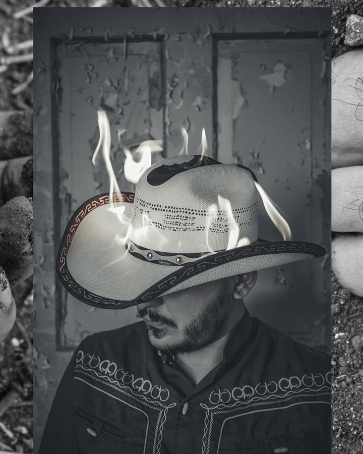 a black and white photo of a man hiding his face with a cowboy hat in flames